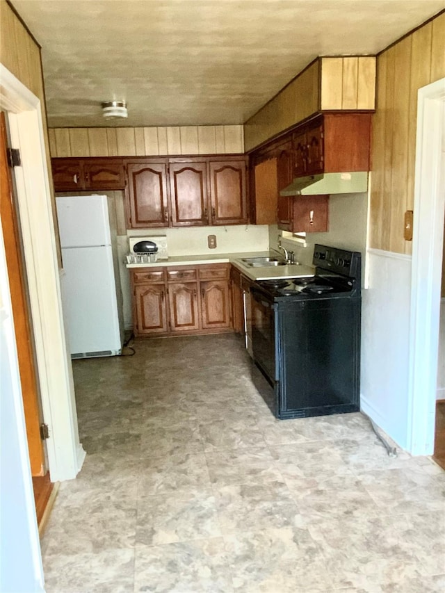 kitchen featuring black electric range oven, a sink, freestanding refrigerator, under cabinet range hood, and light floors