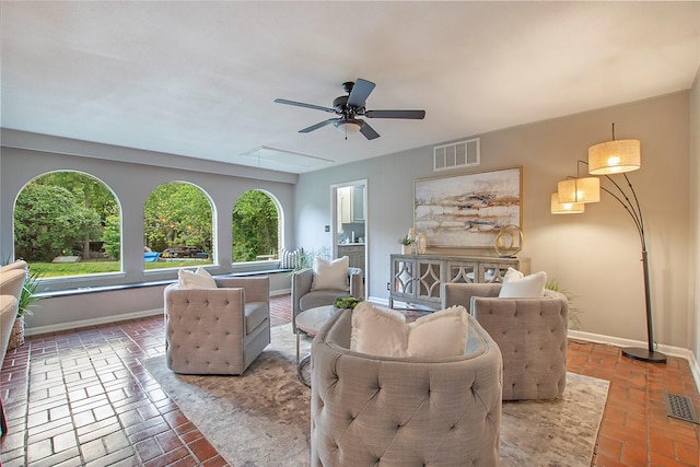 living area with visible vents, baseboards, attic access, brick floor, and a ceiling fan