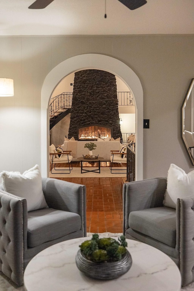 sitting room with a ceiling fan, arched walkways, and a fireplace