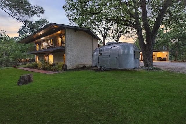 property exterior at dusk featuring a yard, fence, and a balcony
