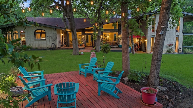 rear view of house with a yard, brick siding, a fire pit, and a wooden deck