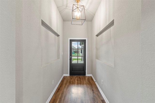 entryway featuring dark wood-style floors, baseboards, a notable chandelier, and a textured wall