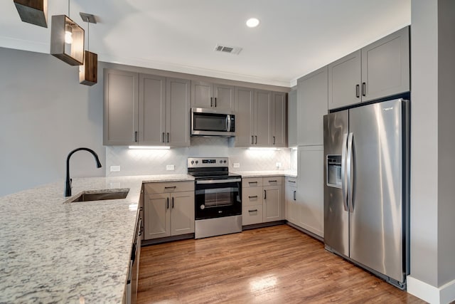 kitchen with appliances with stainless steel finishes, light stone counters, gray cabinets, and a sink