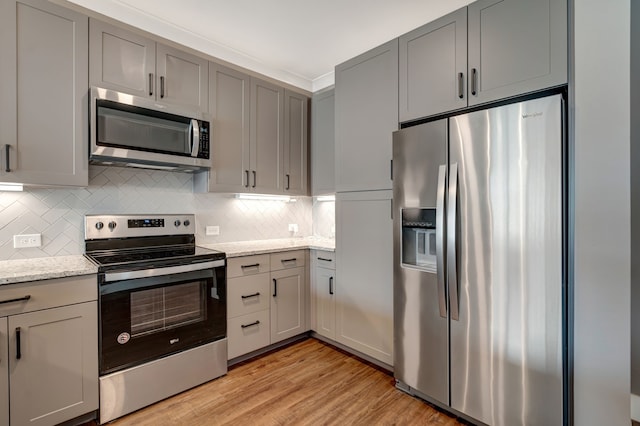 kitchen featuring gray cabinets, light stone countertops, light wood-style flooring, appliances with stainless steel finishes, and backsplash