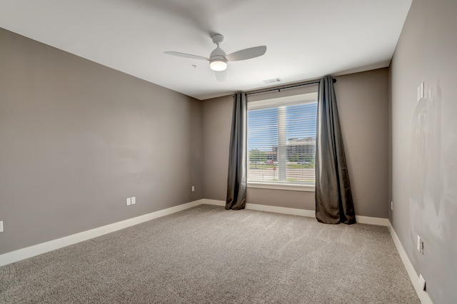empty room featuring light colored carpet, visible vents, a ceiling fan, and baseboards