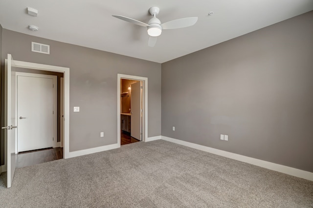 unfurnished bedroom featuring connected bathroom, dark colored carpet, baseboards, visible vents, and a ceiling fan