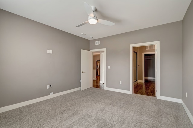 unfurnished bedroom with a walk in closet, visible vents, carpet, and baseboards