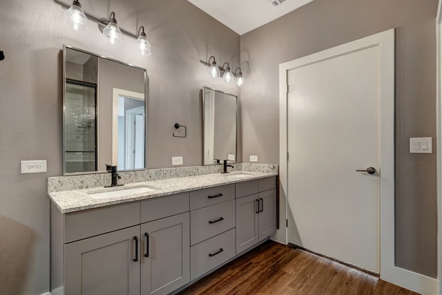 bathroom with double vanity, wood finished floors, tiled shower, and a sink