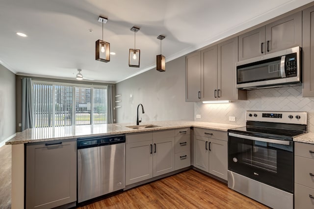kitchen with a sink, gray cabinetry, stainless steel appliances, ornamental molding, and a peninsula