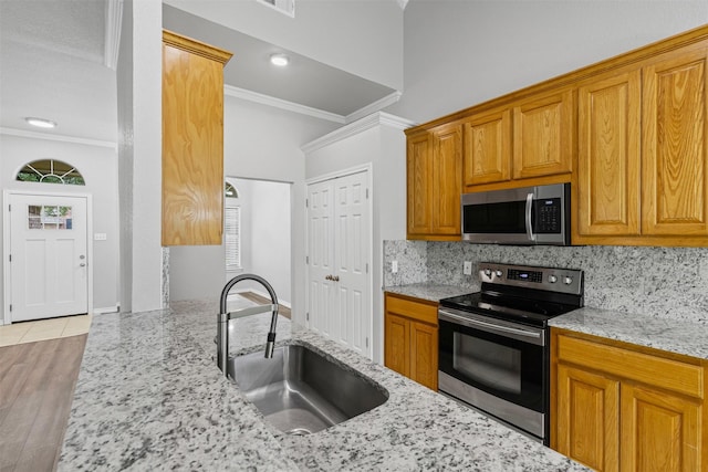 kitchen with crown molding, light stone countertops, appliances with stainless steel finishes, a sink, and tasteful backsplash