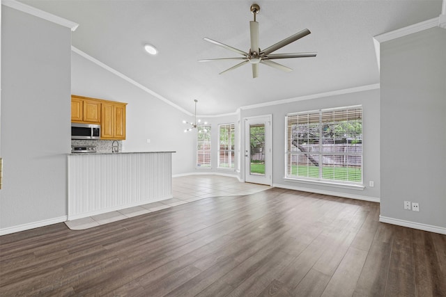unfurnished living room featuring lofted ceiling, wood finished floors, baseboards, a sink, and ceiling fan with notable chandelier