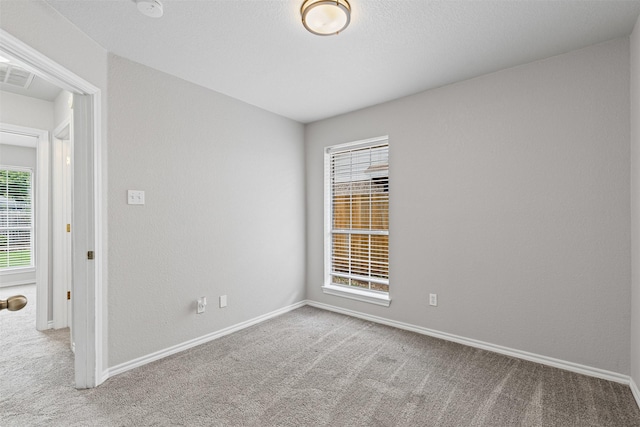 carpeted spare room featuring baseboards, visible vents, and a wealth of natural light