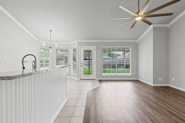 unfurnished living room featuring crown molding, baseboards, ceiling fan with notable chandelier, and a healthy amount of sunlight