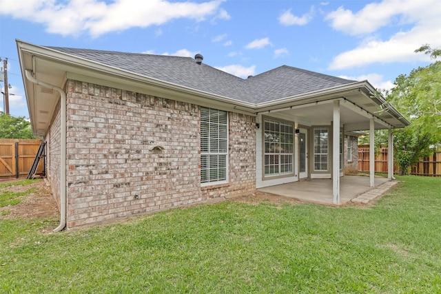 back of house featuring fence, a patio, roof with shingles, brick siding, and a yard