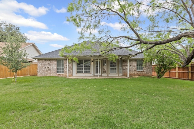 back of property featuring brick siding, a fenced backyard, a lawn, and roof with shingles
