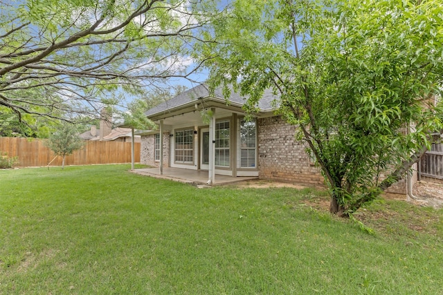 rear view of house with roof with shingles, brick siding, a fenced backyard, a yard, and a patio