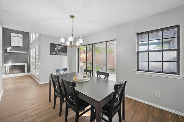 dining area featuring wood finished floors, an inviting chandelier, a fireplace, baseboards, and a textured ceiling
