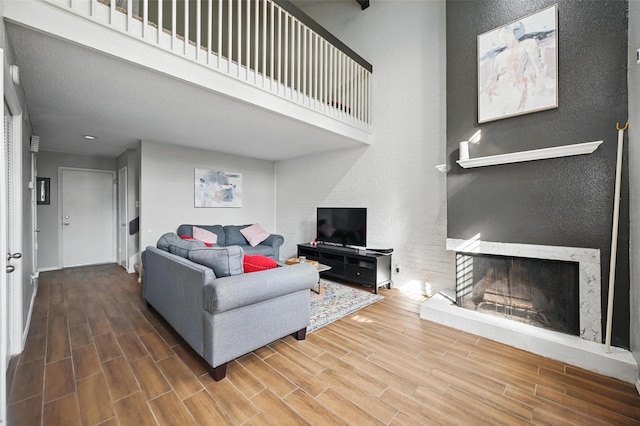 living area featuring a fireplace with raised hearth, a towering ceiling, a textured wall, and wood finished floors