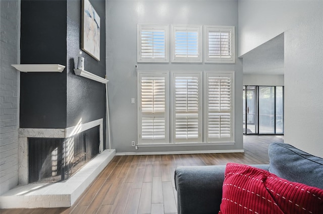 living room featuring a brick fireplace, a high ceiling, wood finished floors, and baseboards