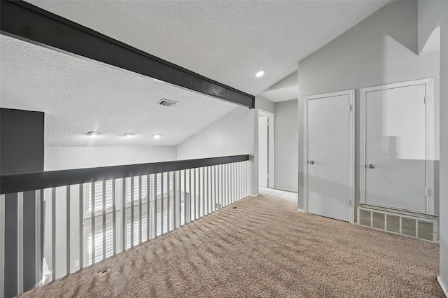 hallway featuring visible vents, a textured ceiling, carpet floors, and vaulted ceiling