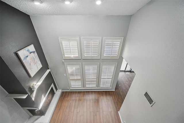 unfurnished living room with baseboards, visible vents, wood finished floors, and a textured ceiling