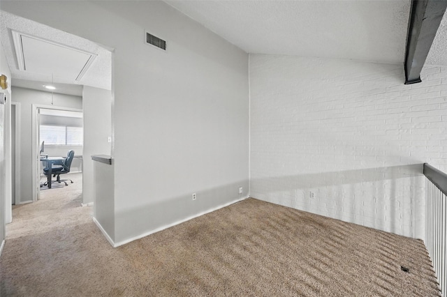 empty room with carpet floors, vaulted ceiling, attic access, visible vents, and a textured ceiling