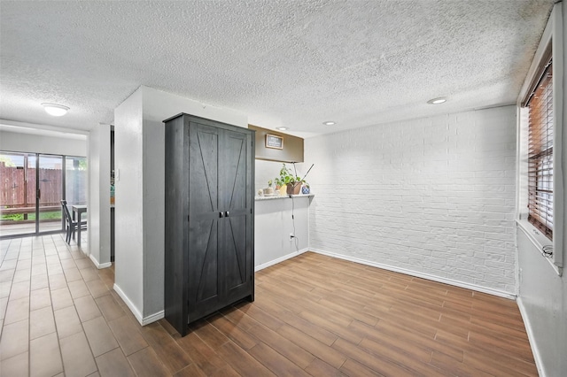 interior space with baseboards, dark wood-type flooring, a textured ceiling, and brick wall
