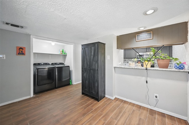 kitchen featuring washing machine and clothes dryer, tasteful backsplash, visible vents, baseboards, and wood finished floors