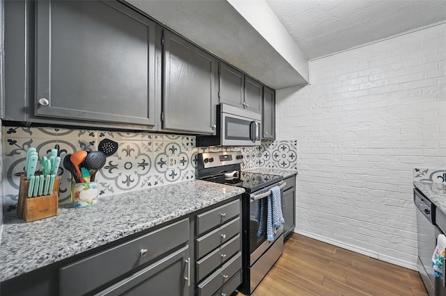 kitchen featuring appliances with stainless steel finishes, dark wood-style flooring, light stone counters, and baseboards