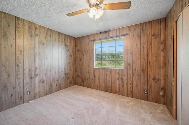 carpeted empty room with wooden walls, a textured ceiling, and ceiling fan