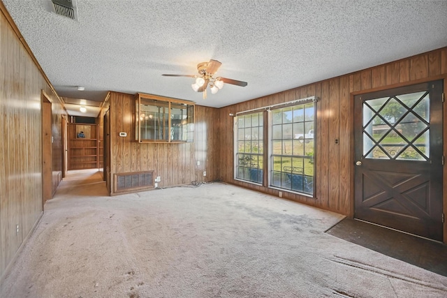 unfurnished living room with visible vents, ceiling fan, wooden walls, and carpet flooring