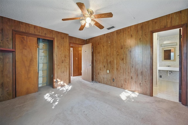 unfurnished bedroom featuring ceiling fan, visible vents, wood walls, a textured ceiling, and carpet floors