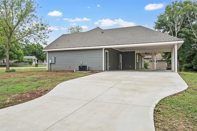 rear view of house featuring driveway, an attached carport, a shingled roof, a yard, and central AC