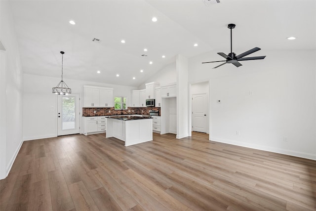 kitchen with open floor plan, dark countertops, stainless steel microwave, and white cabinetry
