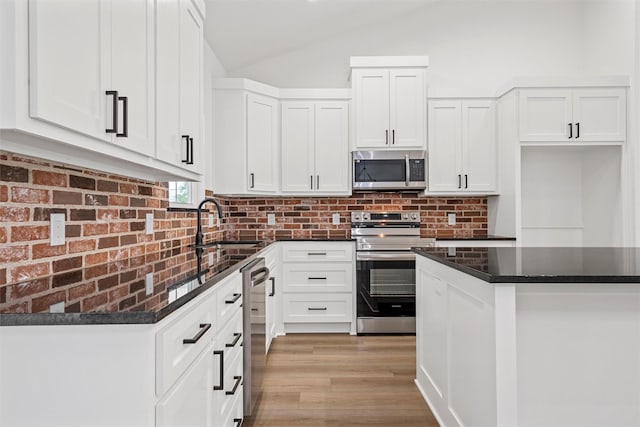 kitchen with lofted ceiling, decorative backsplash, white cabinets, a sink, and appliances with stainless steel finishes