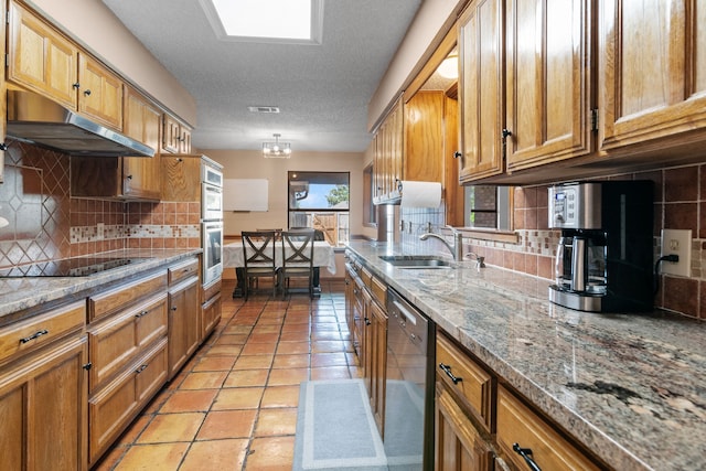 kitchen with under cabinet range hood, brown cabinets, a sink, appliances with stainless steel finishes, and backsplash