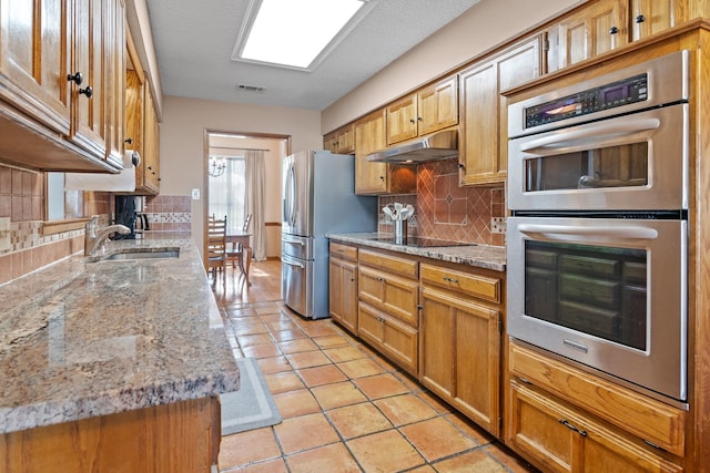 kitchen with a sink, decorative backsplash, appliances with stainless steel finishes, and under cabinet range hood