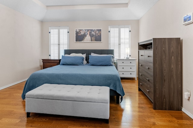 bedroom featuring baseboards, a raised ceiling, wood finished floors, and multiple windows