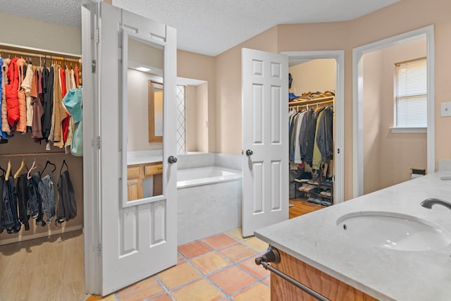 full bathroom with double vanity, a bath, a textured ceiling, a sink, and a spacious closet