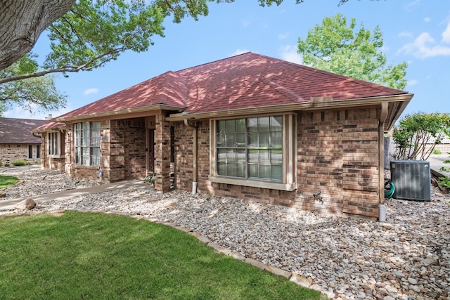 ranch-style house featuring brick siding, a front yard, central AC unit, and roof with shingles