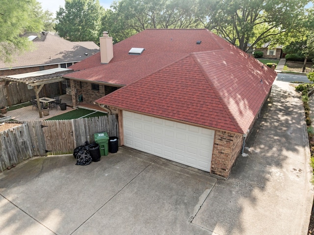 view of side of home featuring concrete driveway, brick siding, fence, and roof with shingles