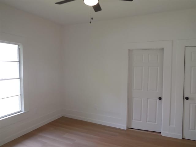 spare room featuring light wood-style floors, a healthy amount of sunlight, a ceiling fan, and baseboards
