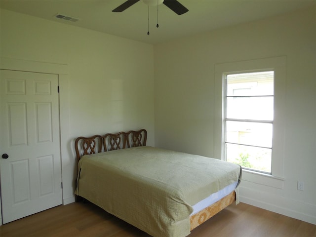 bedroom featuring wood finished floors, a ceiling fan, visible vents, and baseboards
