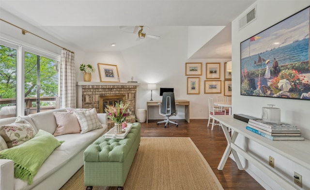 living room featuring dark wood-style flooring, a brick fireplace, a ceiling fan, visible vents, and baseboards