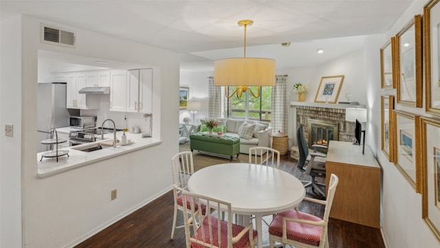 dining room featuring a brick fireplace, visible vents, dark wood-style flooring, and baseboards