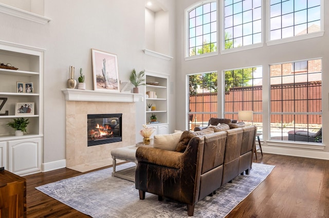 living room featuring dark wood finished floors, built in features, a fireplace, baseboards, and a high ceiling