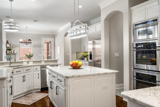 kitchen featuring crown molding, a sink, appliances with stainless steel finishes, a kitchen island, and dark wood finished floors