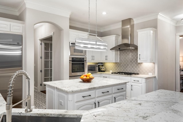 kitchen featuring wall chimney range hood, decorative backsplash, white cabinets, a sink, and stainless steel appliances