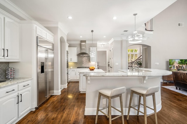 kitchen featuring decorative backsplash, appliances with stainless steel finishes, visible vents, wall chimney exhaust hood, and an island with sink