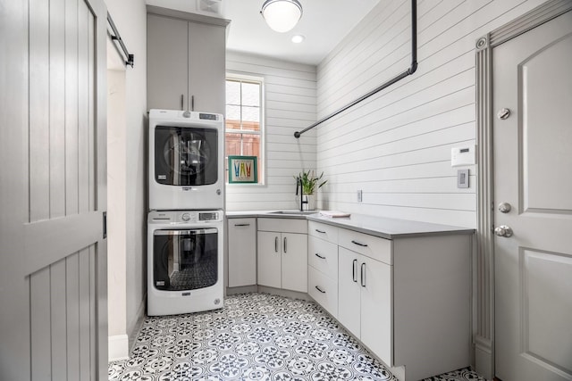 laundry area with wooden walls, a sink, cabinet space, and stacked washing maching and dryer